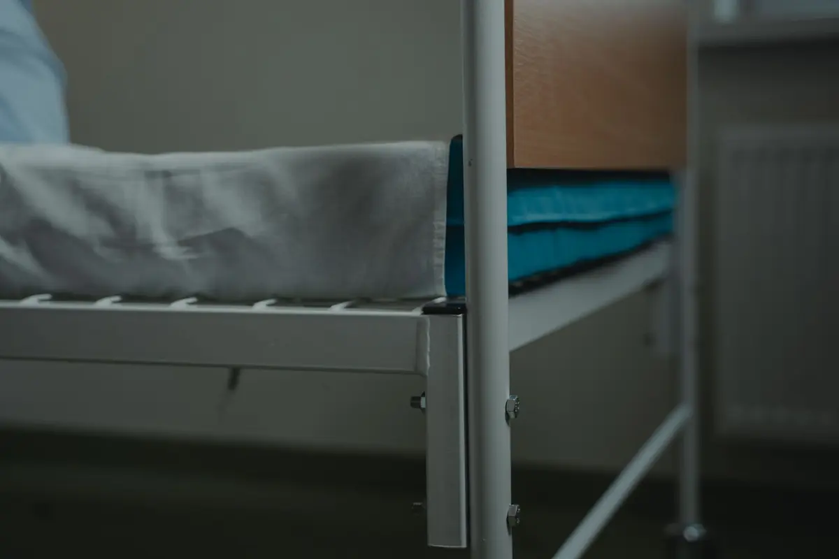 A hand resting on the rail of a hospital bed set up at home